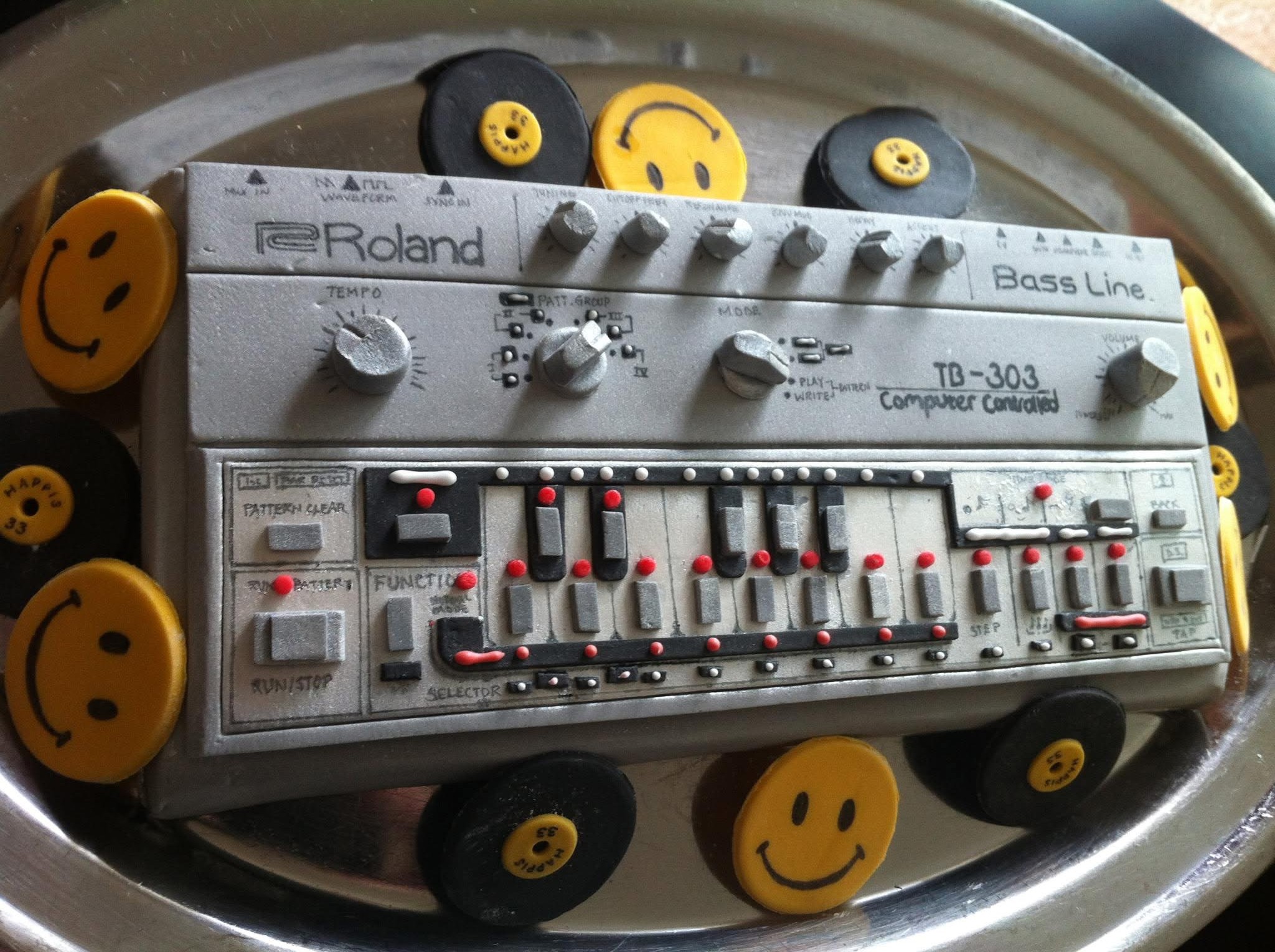 Roland TB-303 cake made for a birthday, edible fondant, on a silver tray surrounded by smiley face and vinyl record decorations